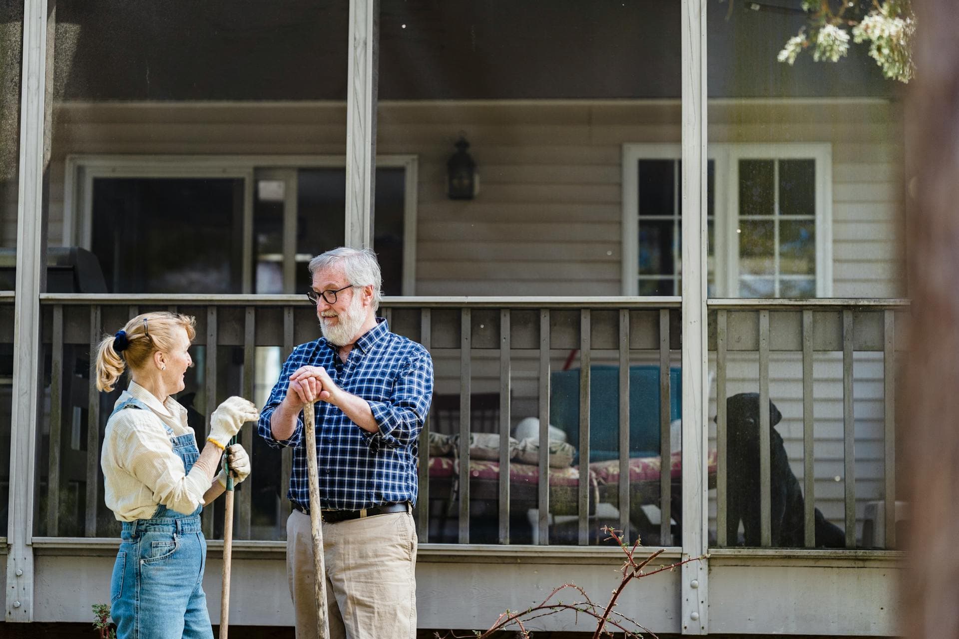 An elderly couple talking to each other while holding gardening tools on a sunny day